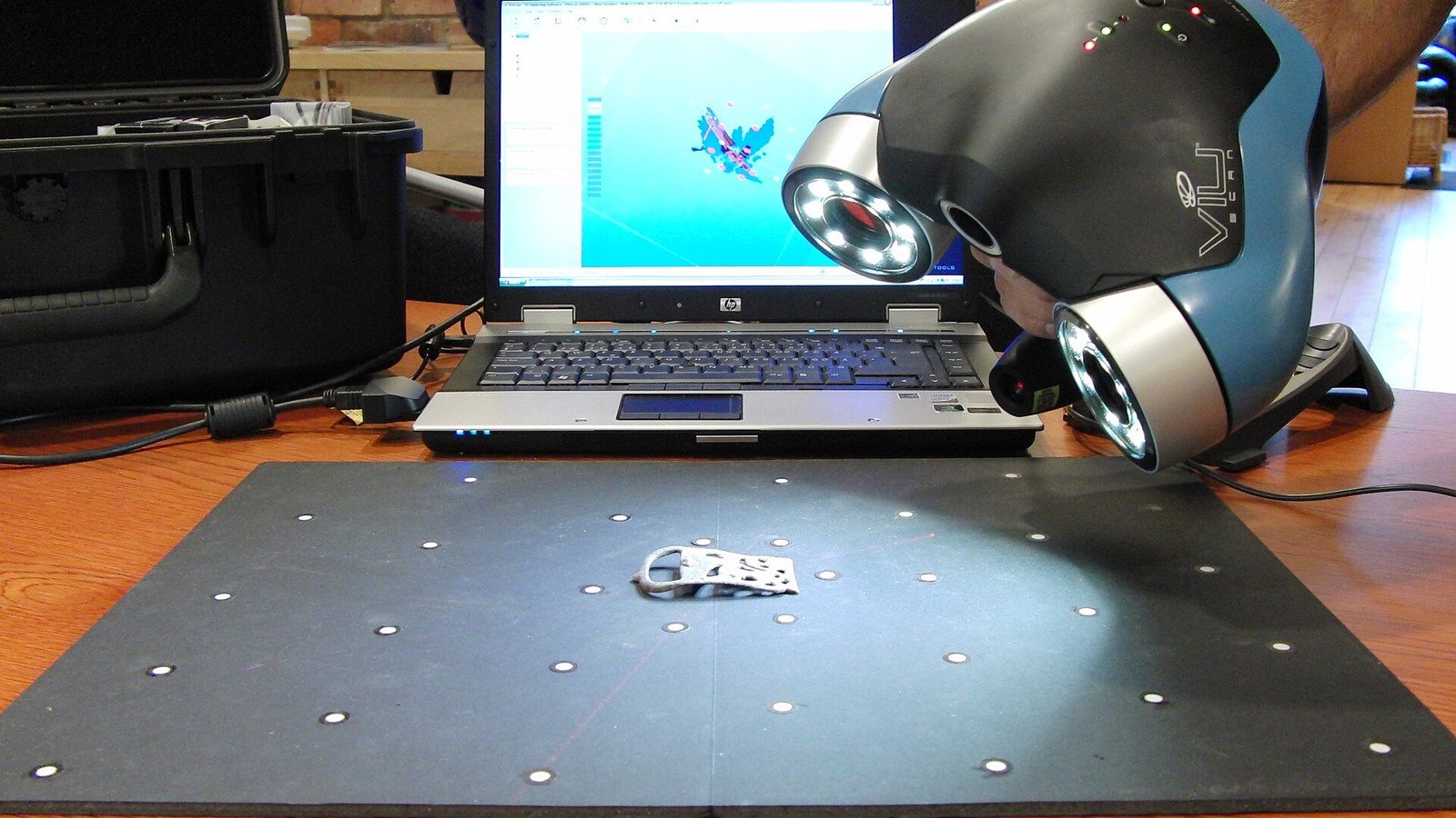 Operator using a handheld 3D scanner to scan an object on a marked platform.